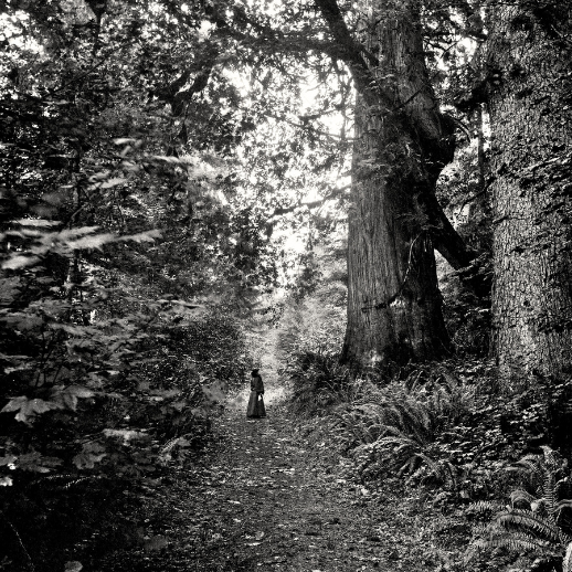 a black and white photo of woman dressed in old-timey dress in the middle of stanley park