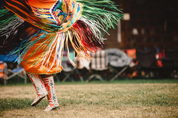 Celebrating Indigenous culture through vibrant powwow dances in BC a photo of the colourful powwow boots and fringed cape in movement as one person dances at a powwow